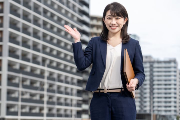 笑顔で片手を上げるスーツ姿の女性の画像