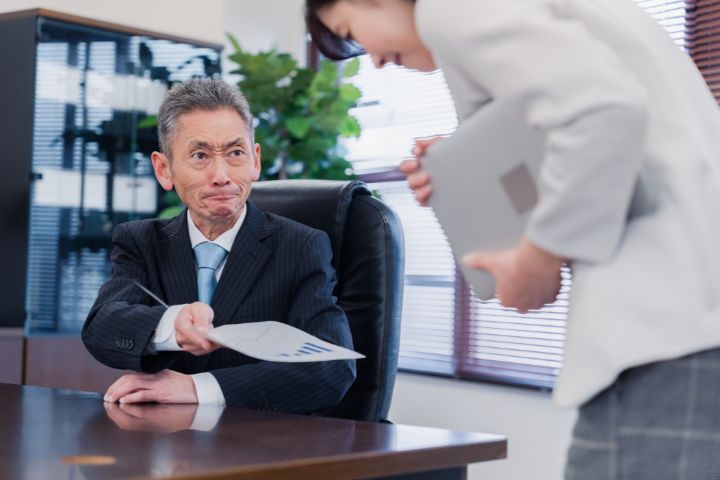 厳しい表情で書類を突き返す男性の画像